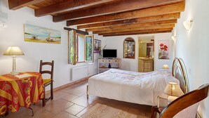 A bedroom with a bed, a chair, a table, a TV, and artwork on the walls. - Bed and Breakfast 'Chambre Double Carpediem Bergerac' with Shared Garden, Wi-Fi and Air Conditioning (Prigonrieux)