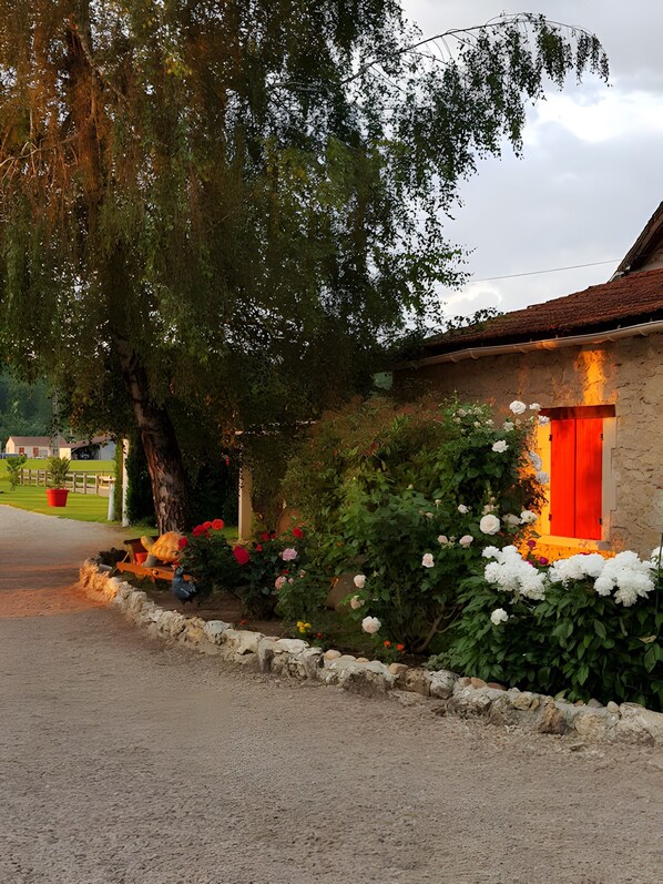 A rustic building with a stone facade, a wooden door, and a garden with various flowers.