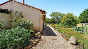 A building with a gravel path leading to a door, surrounded by greenery and a clear sky.