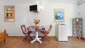 A room with a bed, a dining table with chairs, a television, a refrigerator, and wall decorations.