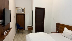 A hotel room with a bed, a desk with a TV, a chair, a wardrobe, and a door. - Hotel AVG Palace (Tijara)