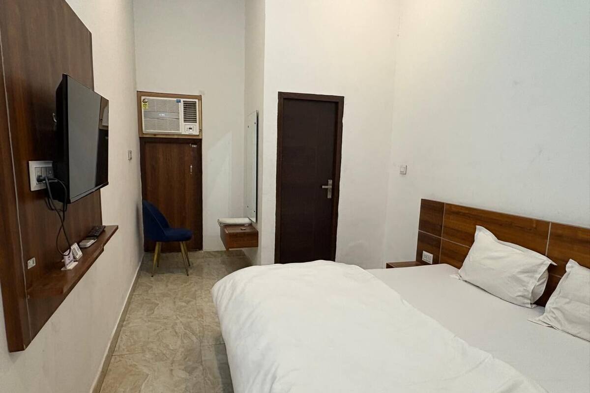 A hotel room with a bed, a desk with a chair, a television, and an air conditioning unit.