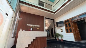 A reception area with a wooden reception desk, a glass balustrade, and a staircase leading to an upper level. - Hotel AVG Palace (Tijara)