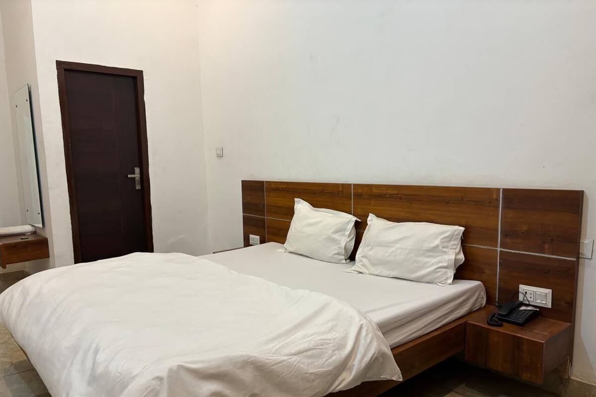 A bedroom with a wooden headboard, two white pillows, a white bedspread, a bedside table with a phone, and a door in the background.