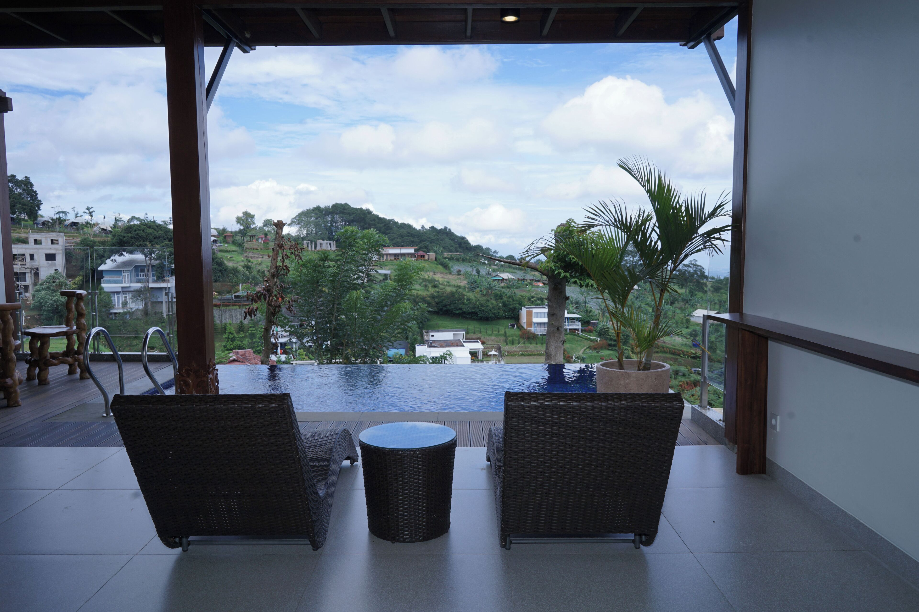 A balcony with wicker furniture, a small round table, and a view of a swimming pool and surrounding greenery.