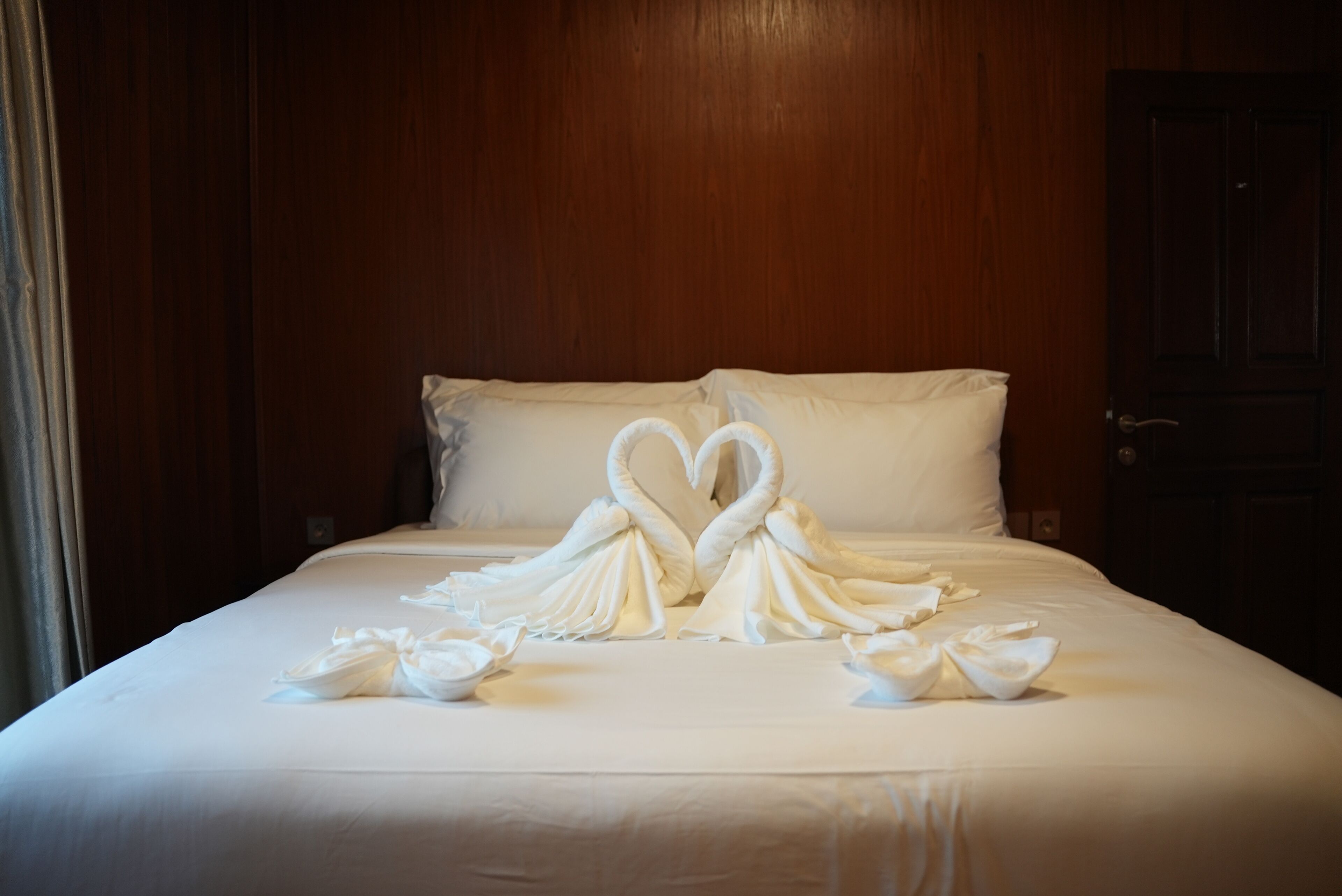 A hotel room with a neatly made bed, wooden headboard, and a dark door.