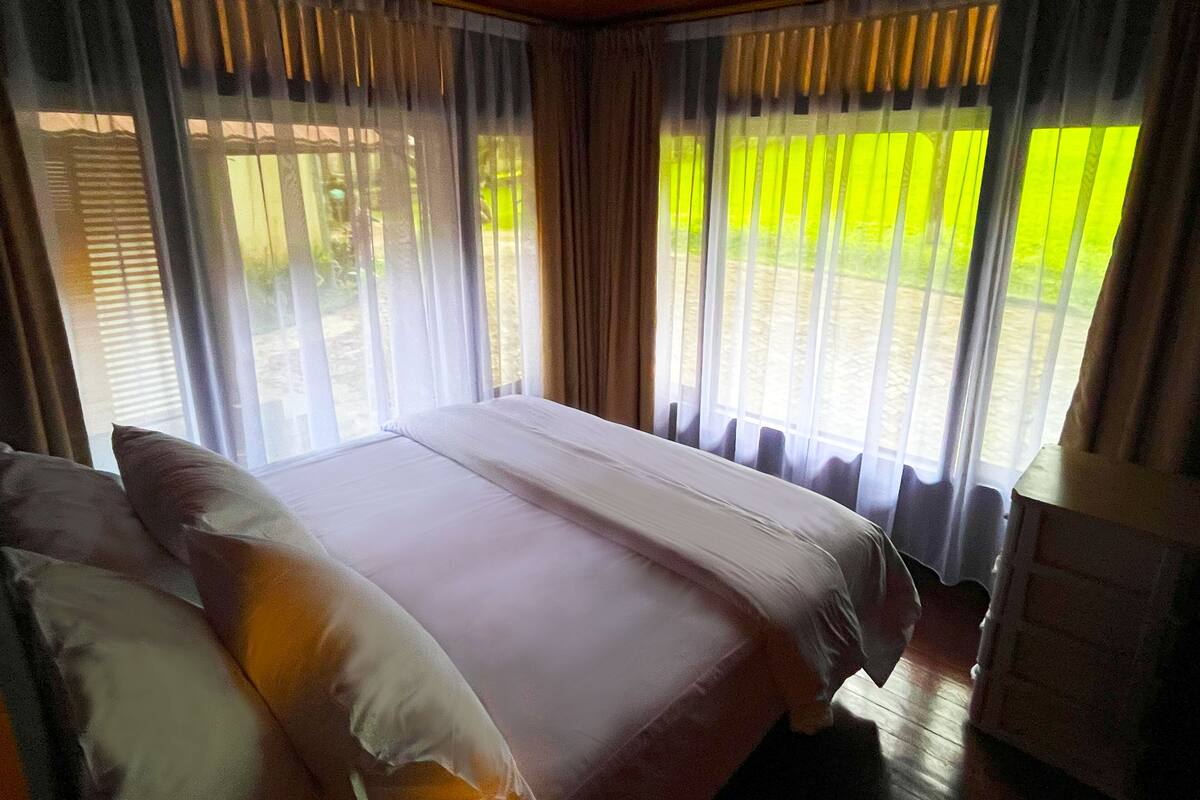 Une chambre à coucher avec un lit, des rideaux et une vue sur la verdure.