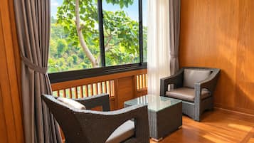 A room with a view of greenery through a window, wicker furniture, and wooden flooring.