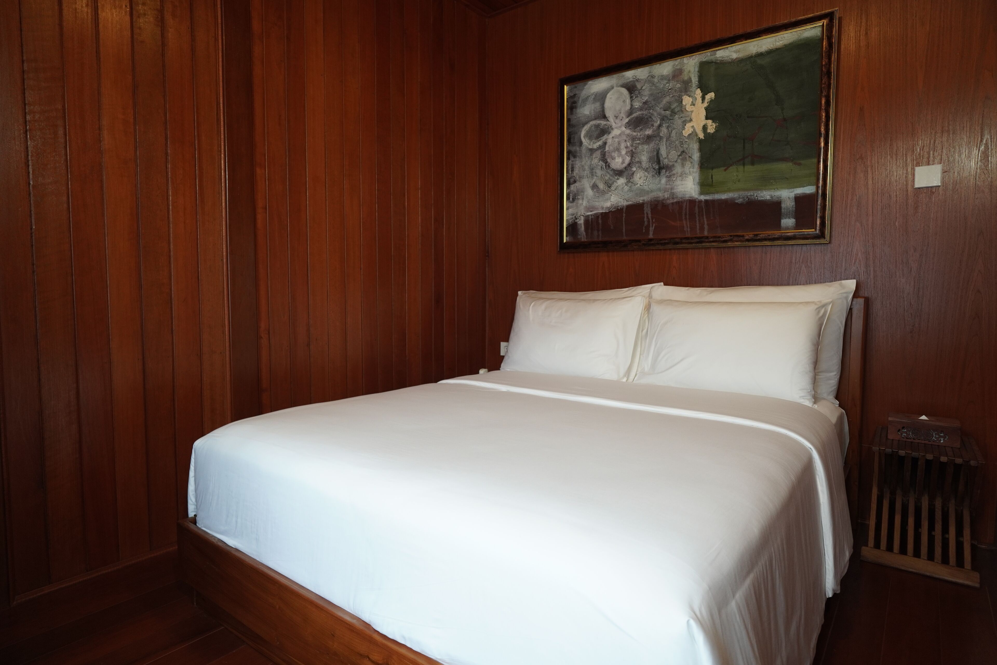 A neatly made bed in a room with wooden paneling and a painting on the wall.
