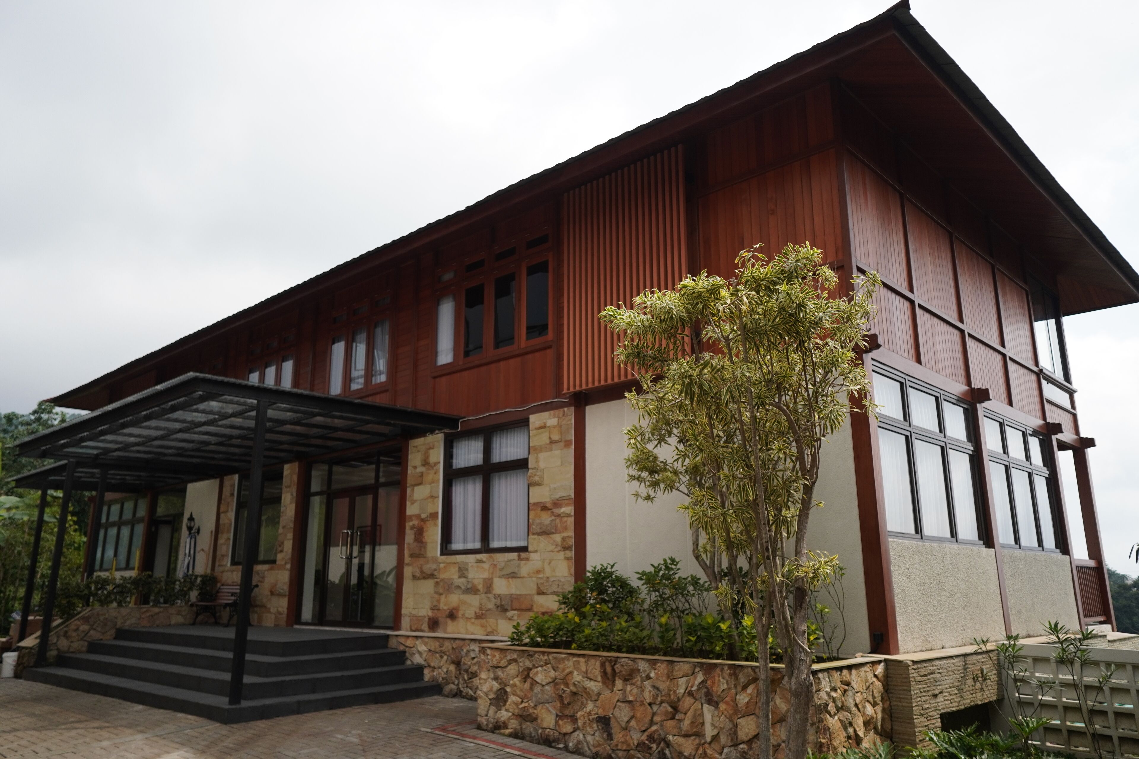 A modern two-story building with a stone facade, large windows, and a covered entrance area.