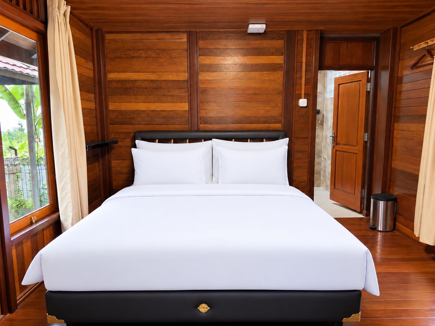 A large bed with white linens, a wooden headboard, and a small bedside table with a lamp.