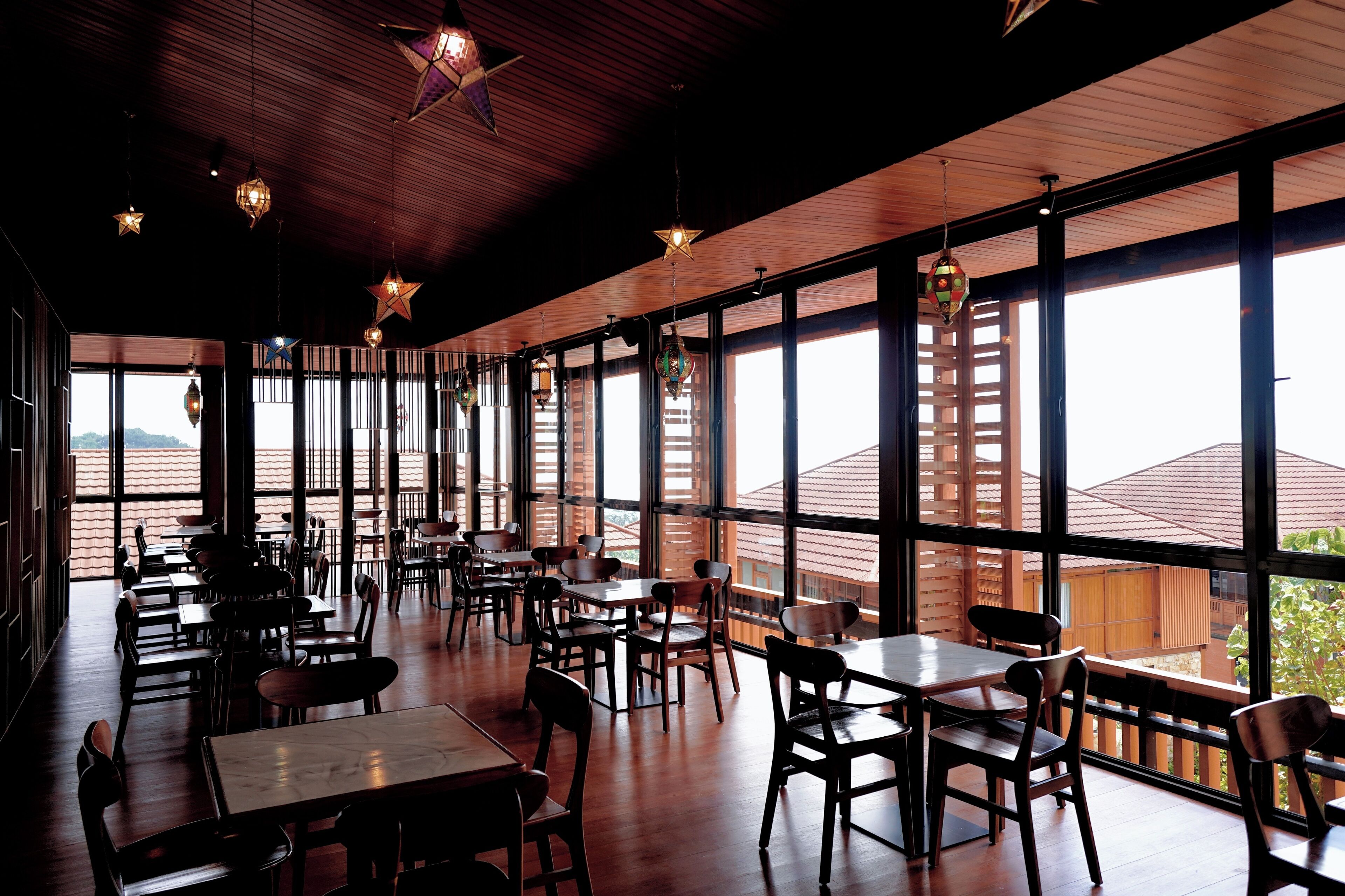 Een restaurant met houten tafels en stoelen, grote ramen en hangende sterrenlampen.