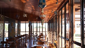 Un restaurant spacieux avec des tables et des chaises en bois, de grandes fenêtres et des éléments décoratifs suspendus.