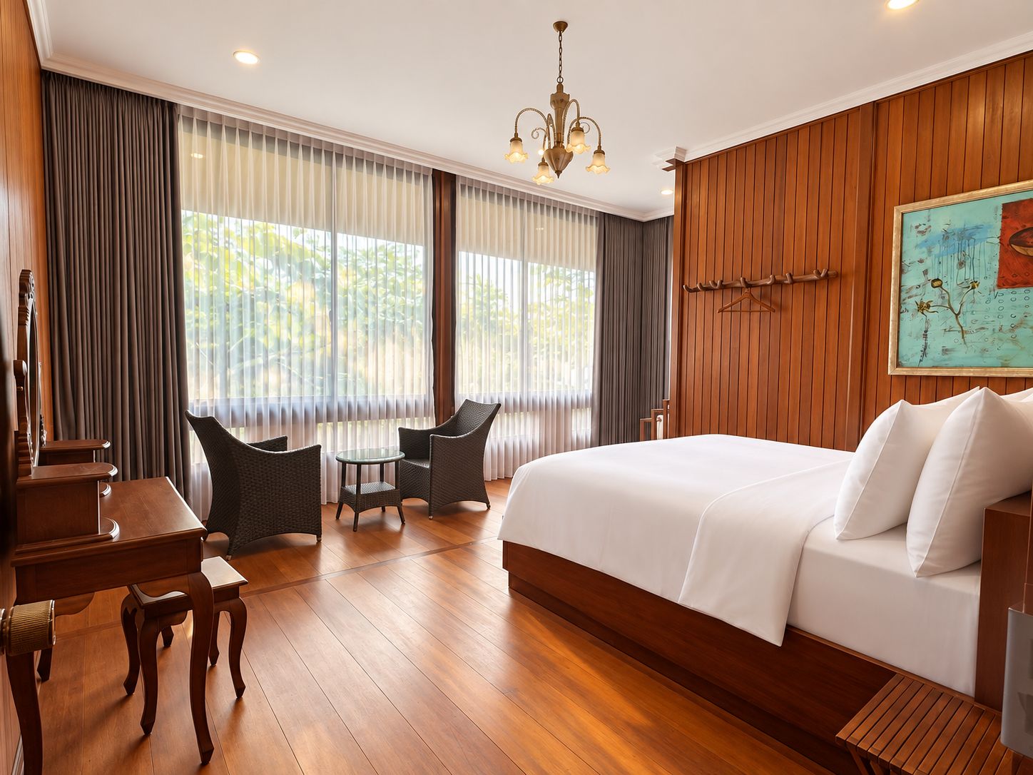 A hotel room with a large bed, wooden flooring, a desk with chairs, and a chandelier.