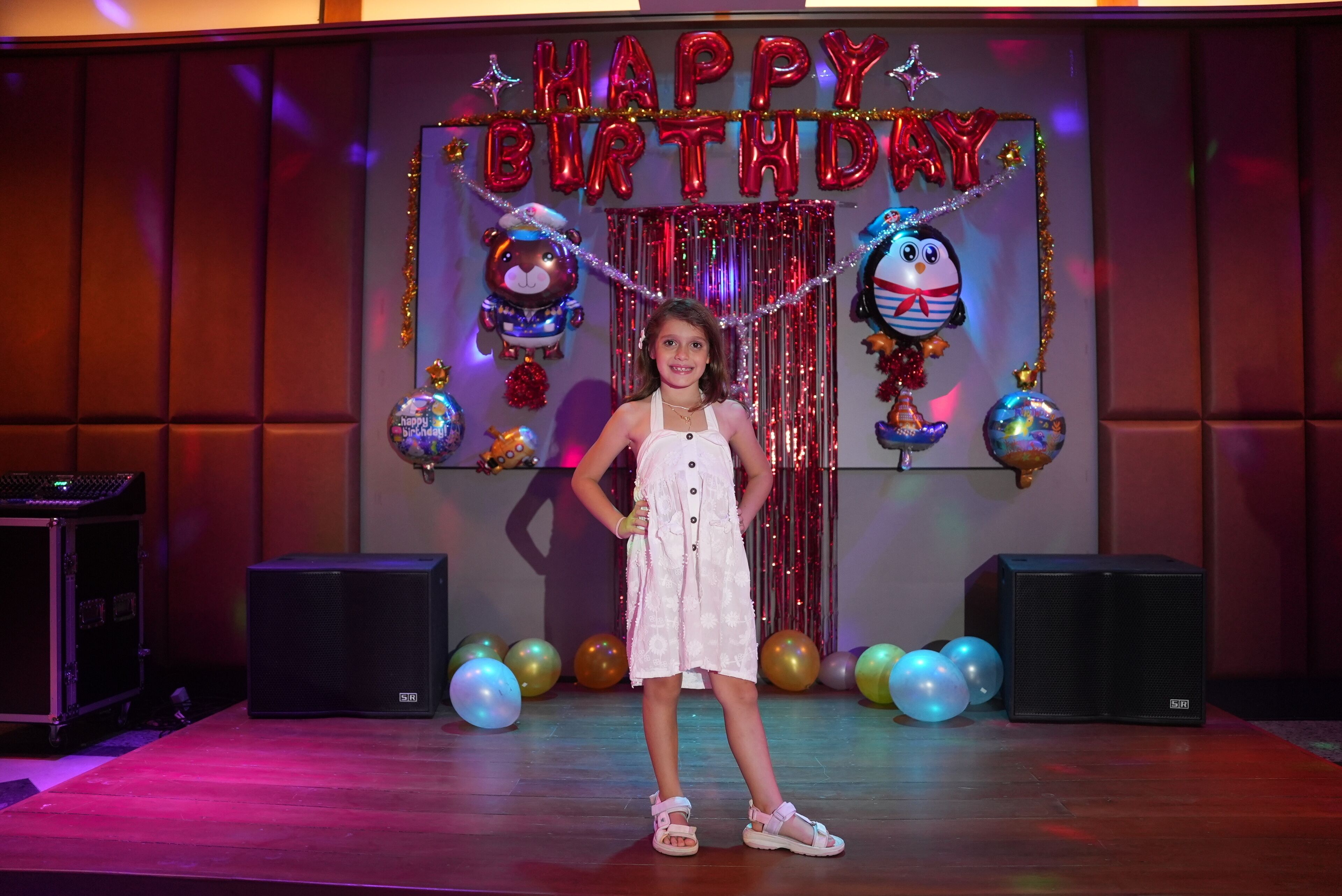Een podium met een 'Happy Birthday' achtergrond, ballonnen en een microfoon.