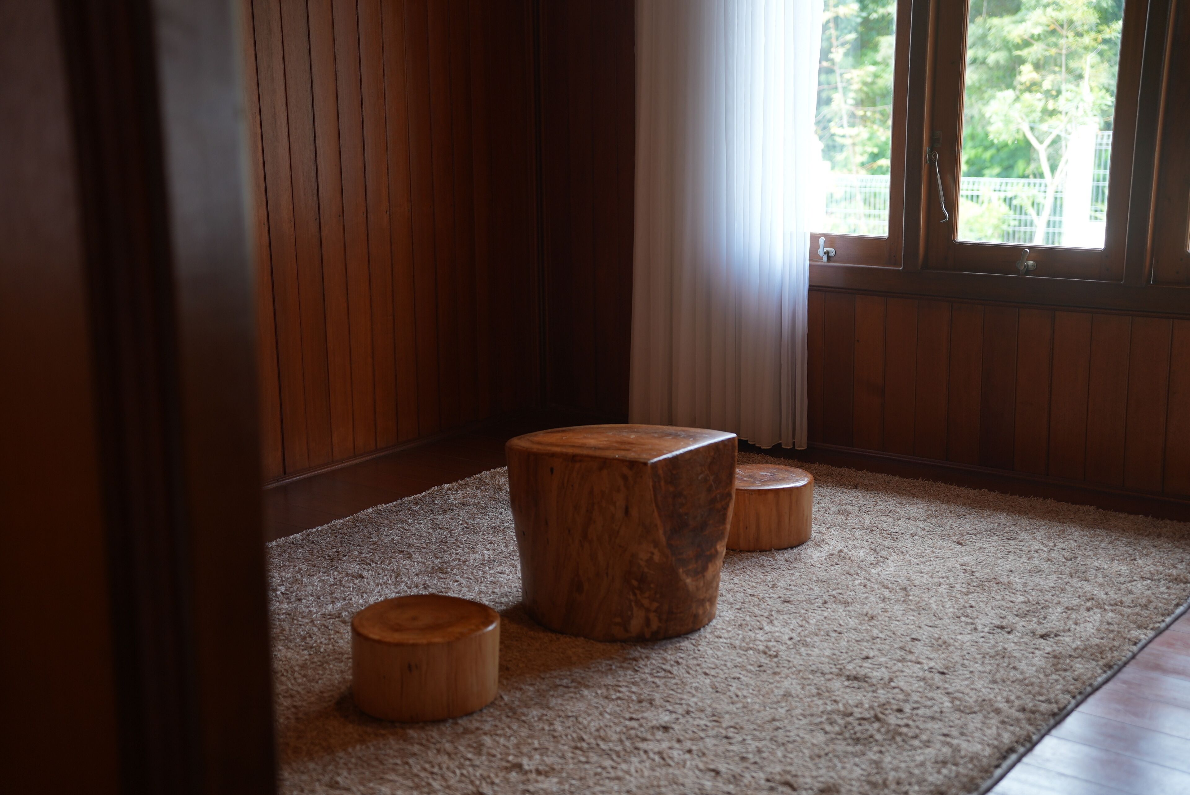 A room with a large window, wooden flooring, and three wooden stools.