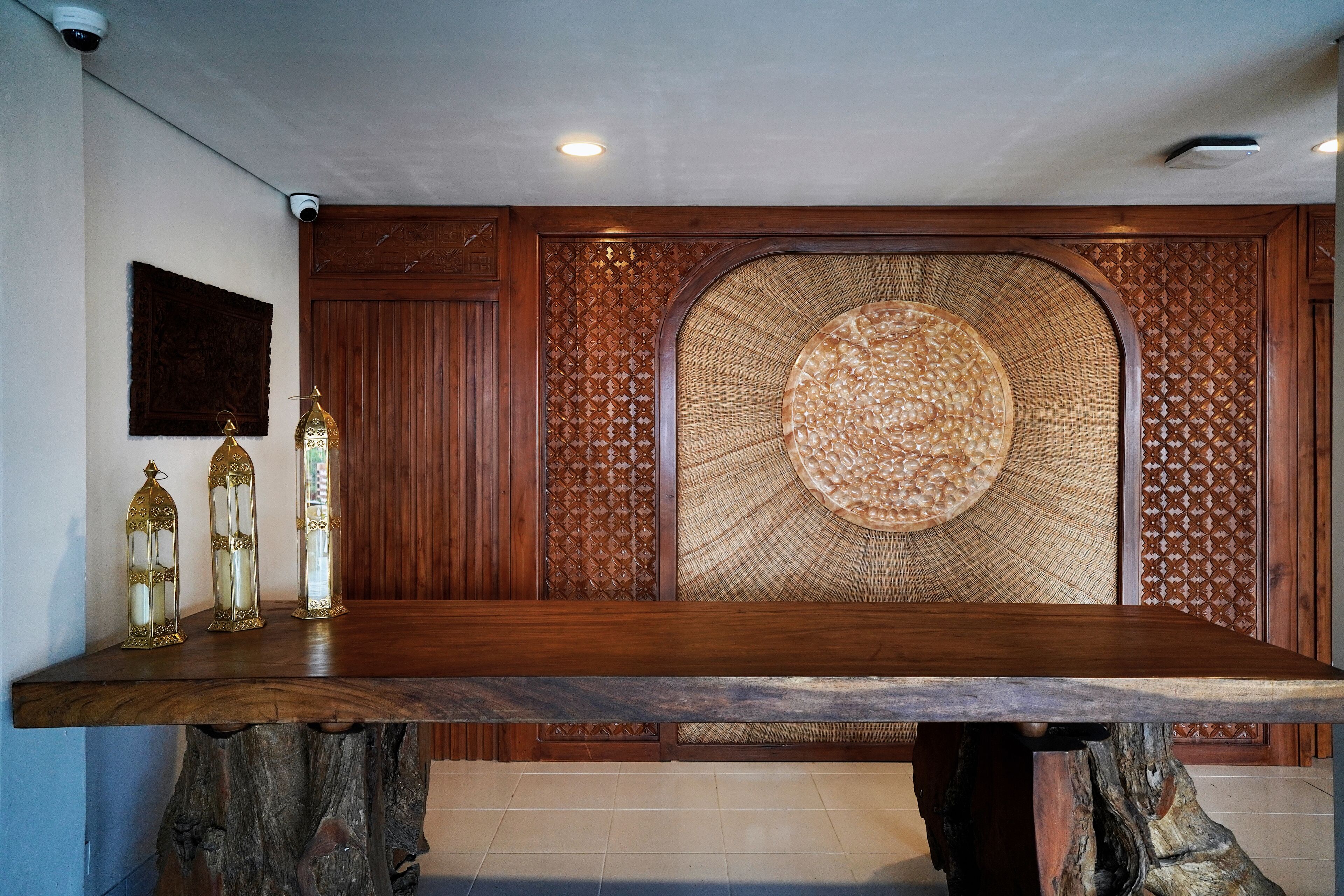 A wooden dining table with a unique woven backrest, three decorative candle holders, and a wall-mounted security camera.