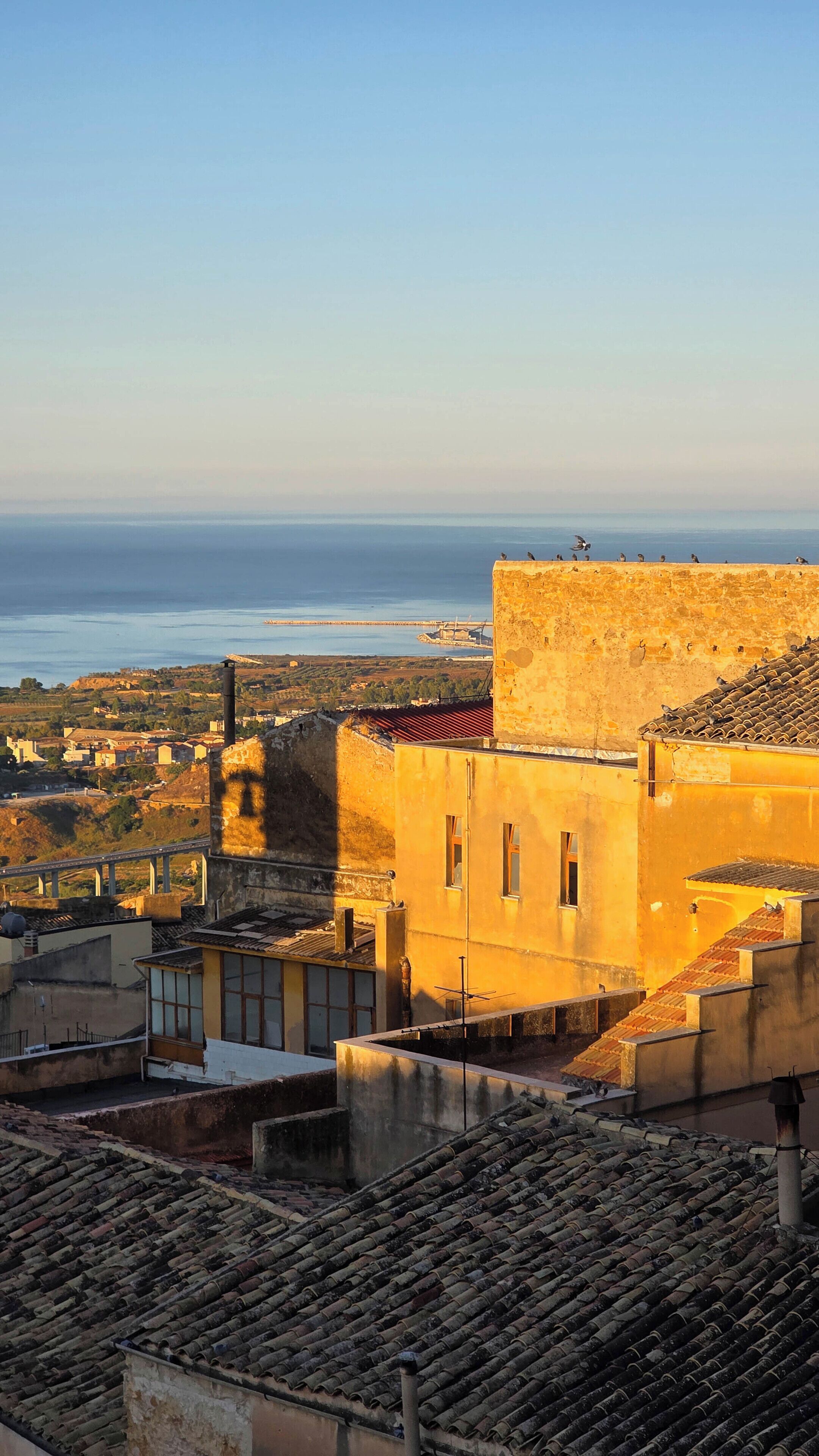 Un pueblo costero con edificios de tejados de teja anaranjada, un muro de piedra destacado y vista al mar.