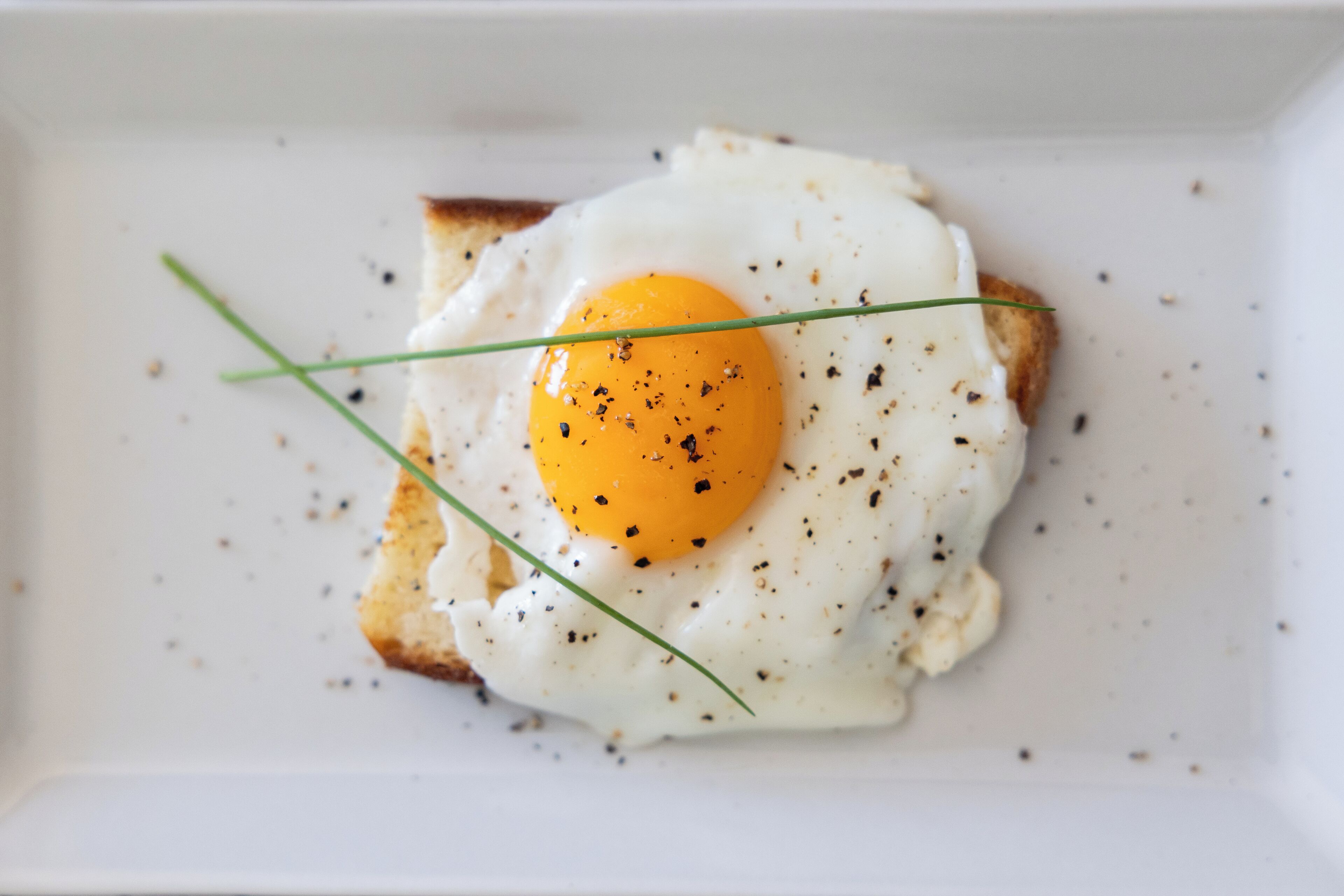 A plate with a fried egg on toast, garnished with chives and black pepper.