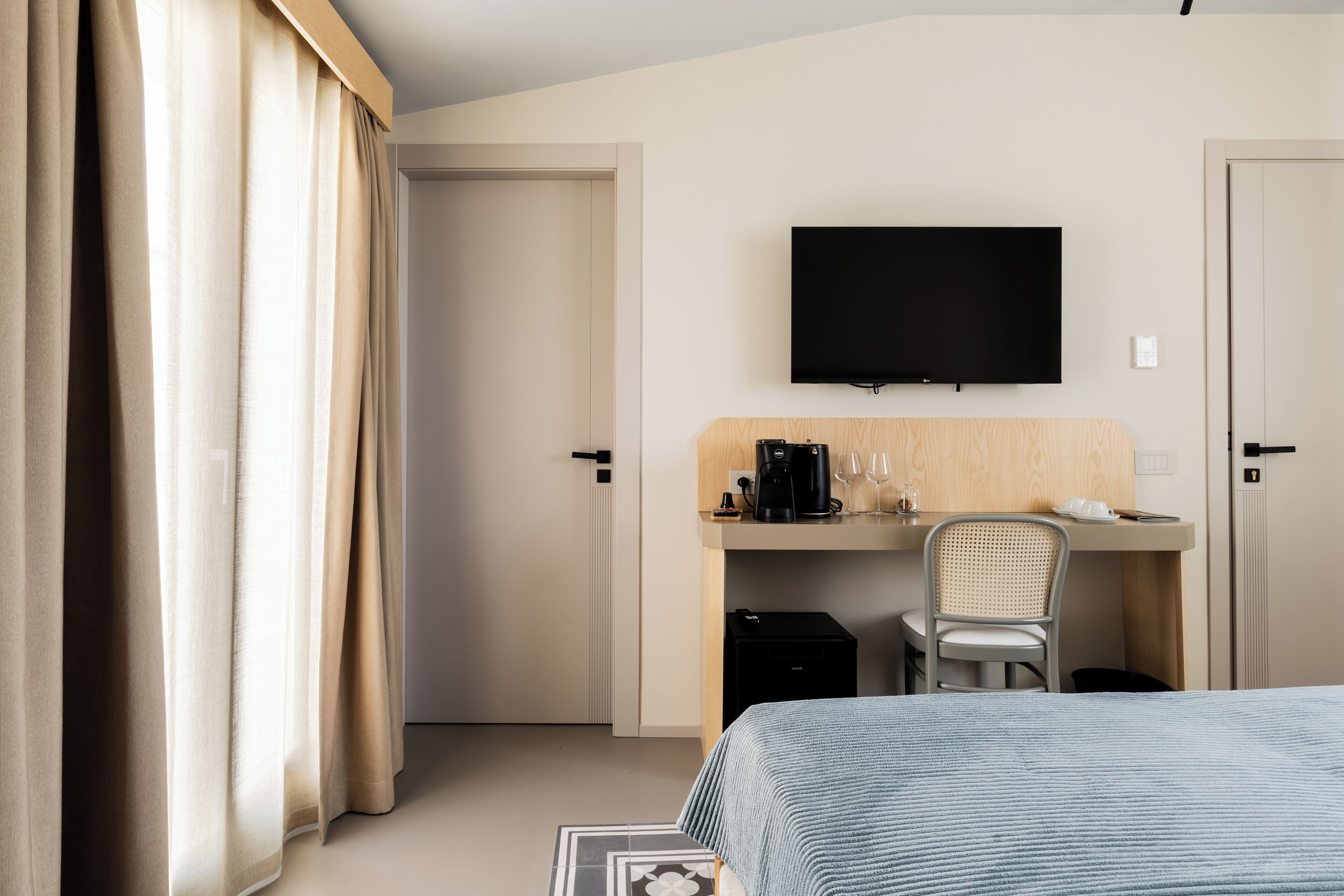 A hotel room with a bed, a desk with a chair, a television, and a coffee machine.