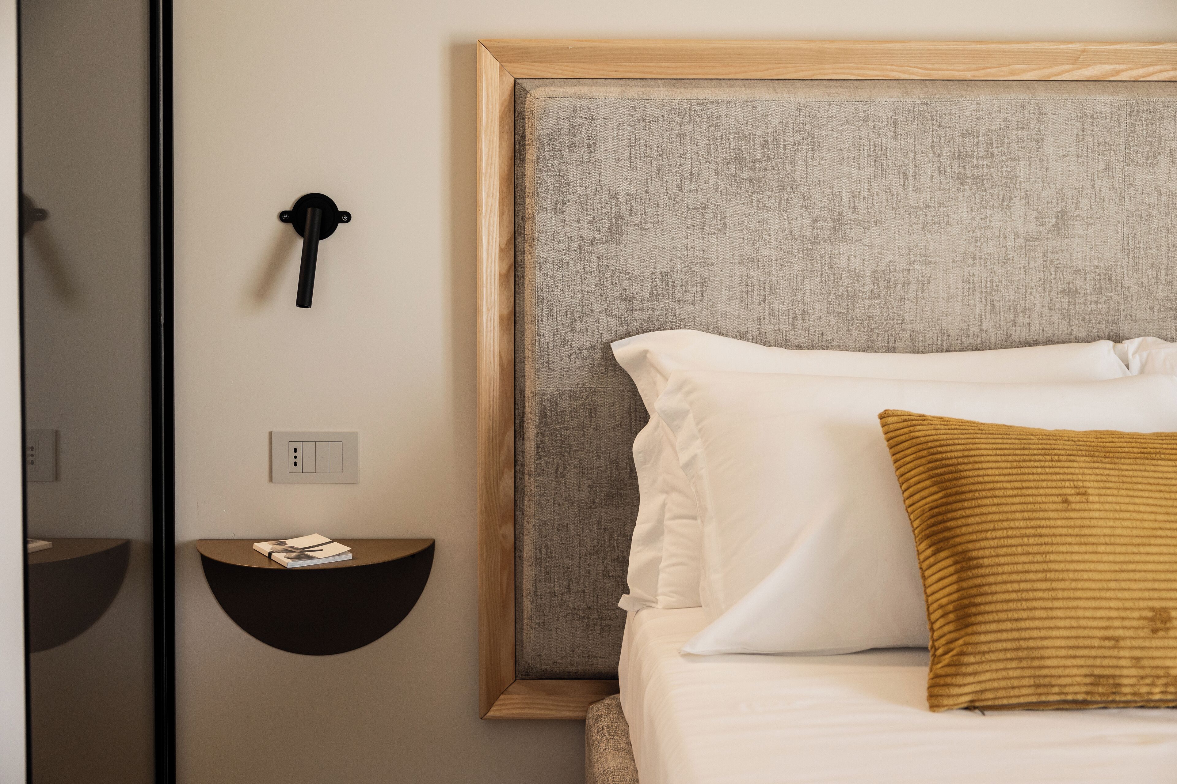 A neatly arranged bedroom with a bed, a bedside table, and a wall-mounted light fixture.