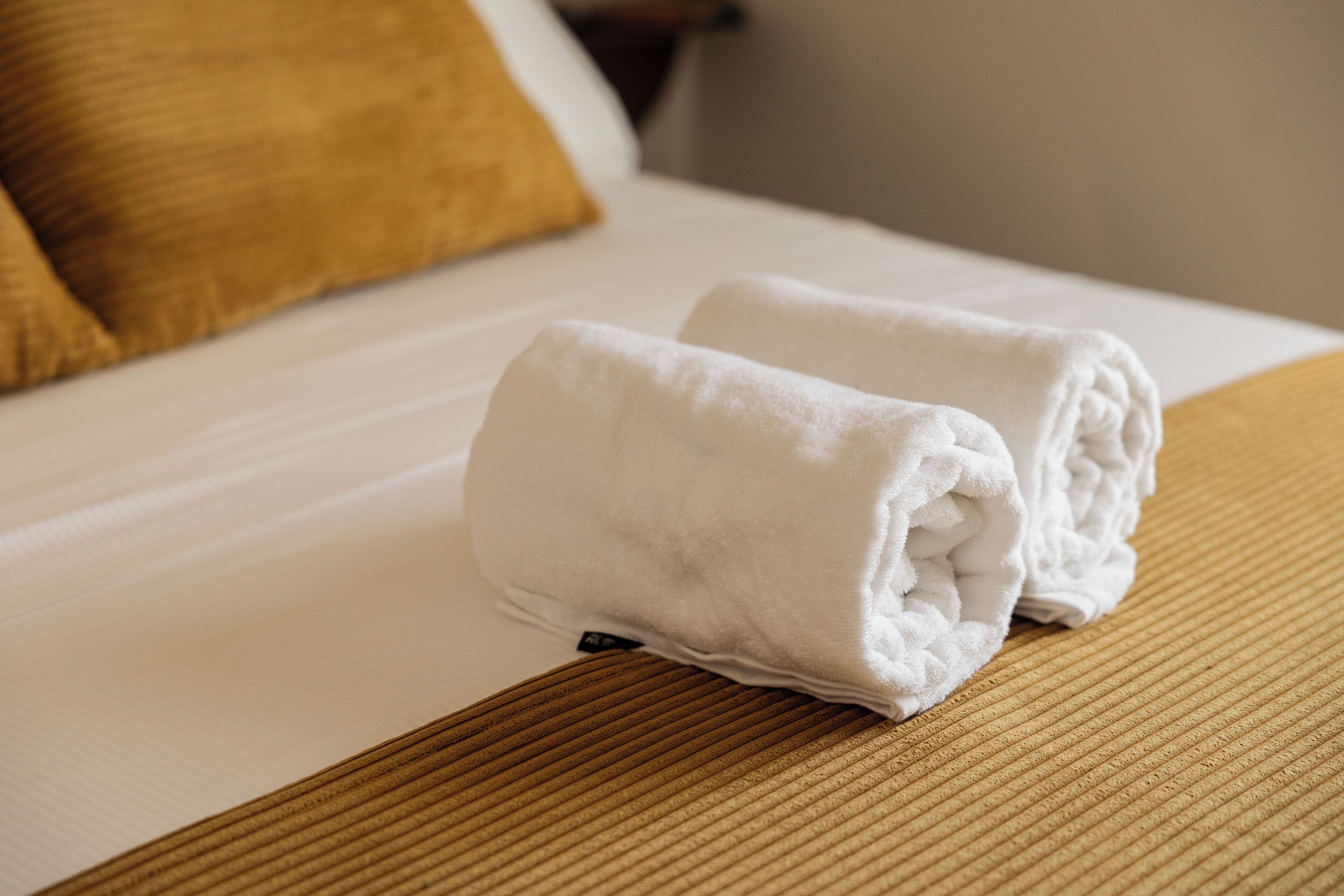 A neatly made bed with two folded white towels on a textured brown bedspread.