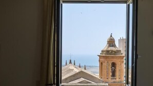 A room with a bed, a window with curtains, and a view of a building with a dome and a statue. - Domus Terravecchia  (Agrigento)