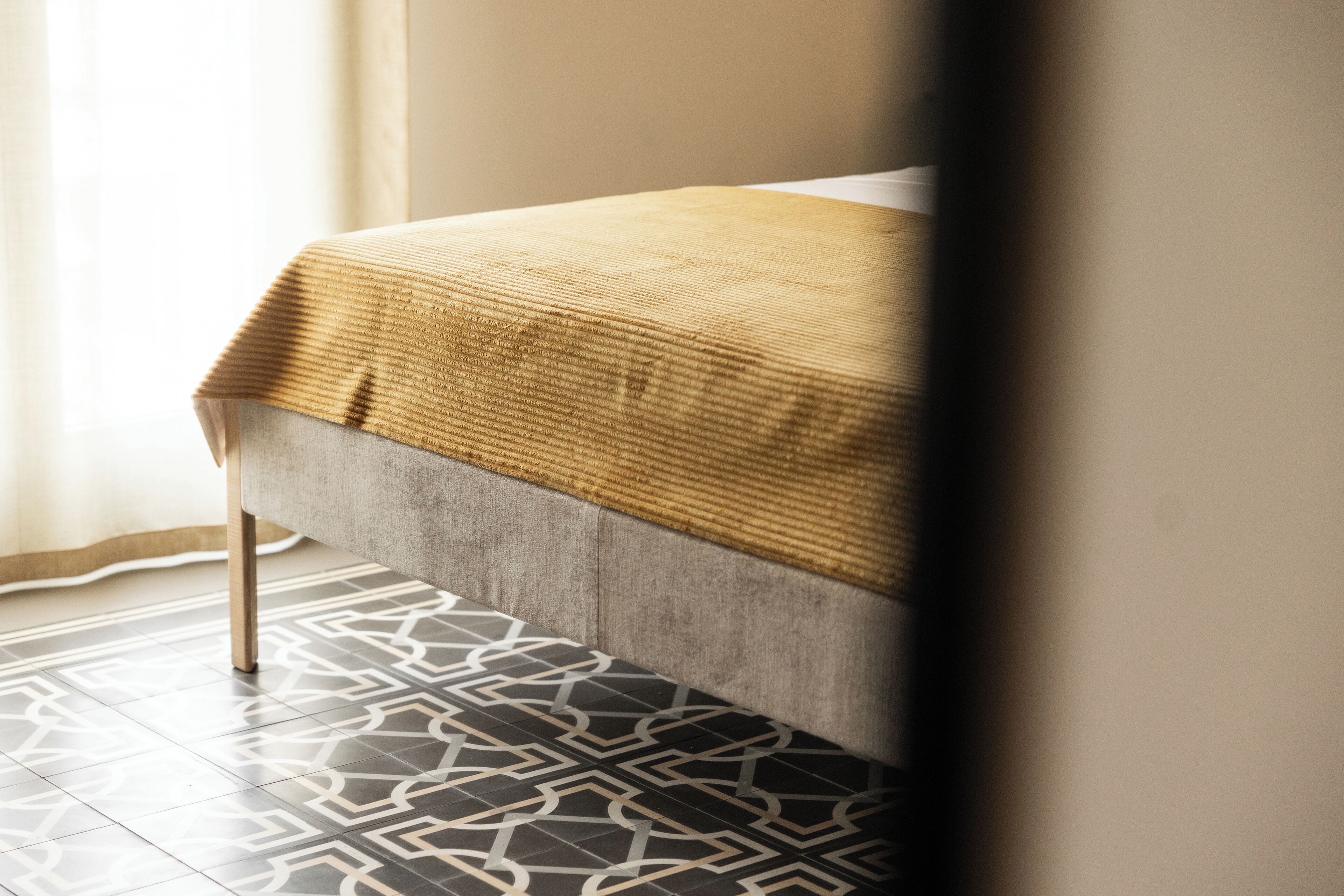 A bed with a textured blanket, a patterned floor, and a curtain.