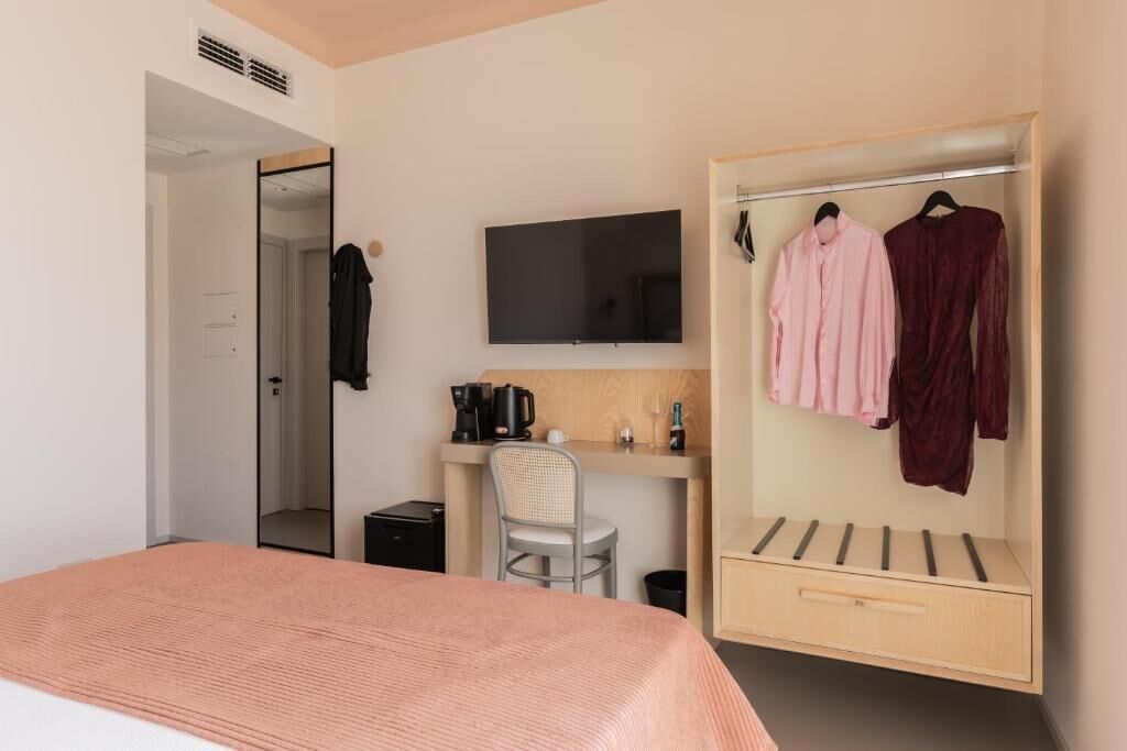 Une chambre d’hôtel moderne comprenant un lit, un bureau avec une télévision, une chaise, une armoire et un petit meuble de rangement.