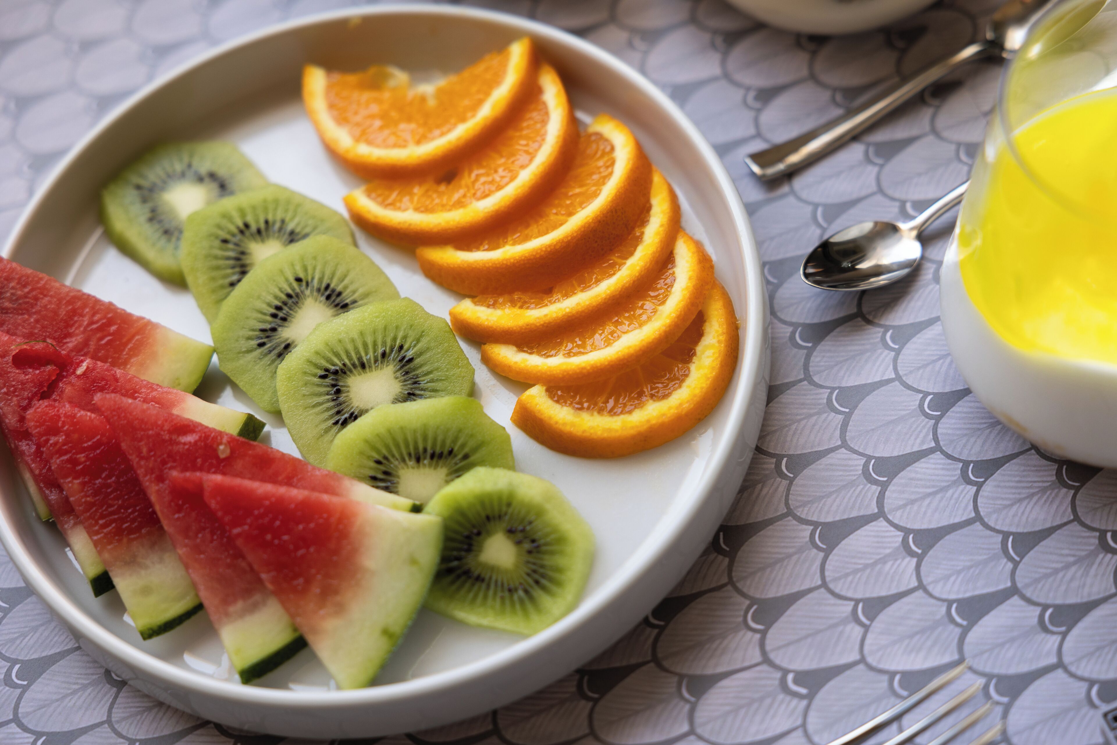 A plate with sliced watermelon, kiwi, and orange on a table with a patterned tablecloth.