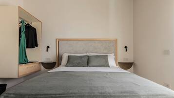 A bedroom with a bed, a wooden headboard, two bedside tables, a mirror, and a hanging green garment.