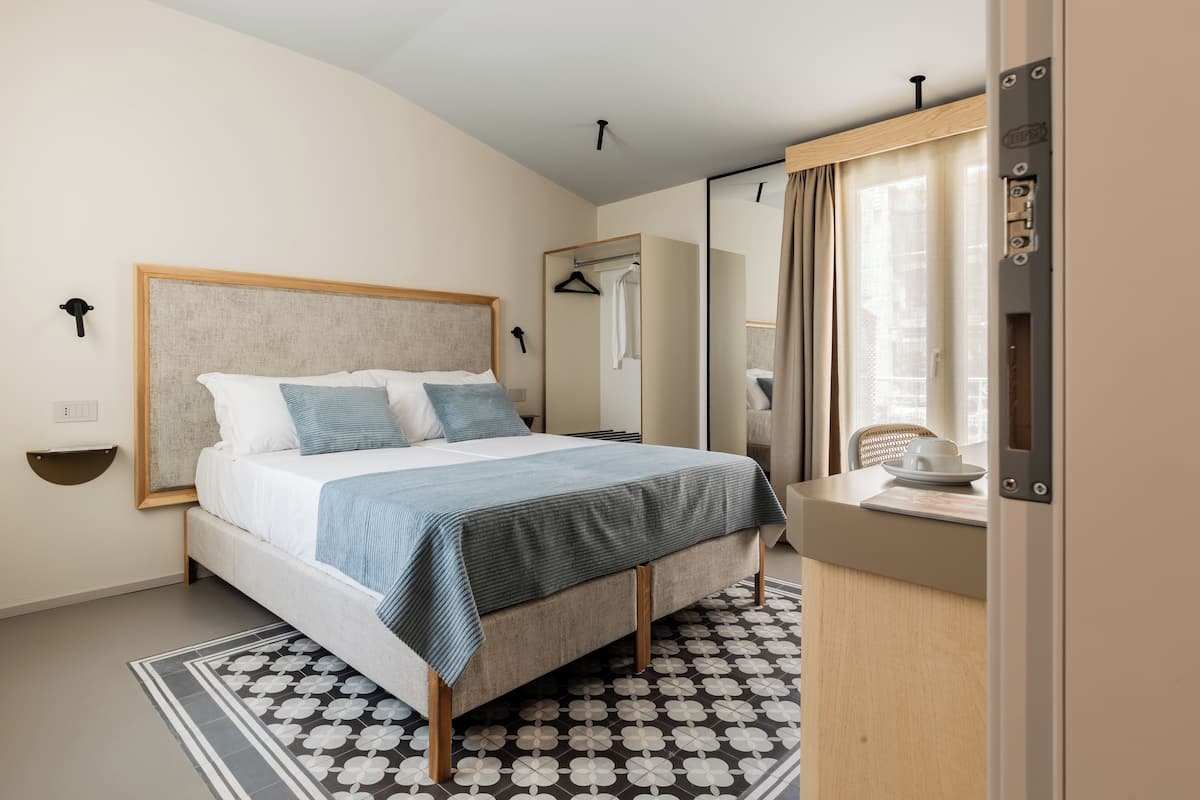 Una camera d'albergo moderna con un letto grande, un comodino, uno specchio e un armadio.