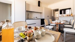 A modern kitchen with white cabinets, a dining area with a table set for breakfast, and a large window providing natural light. - Domus Terravecchia  (Agrigento)