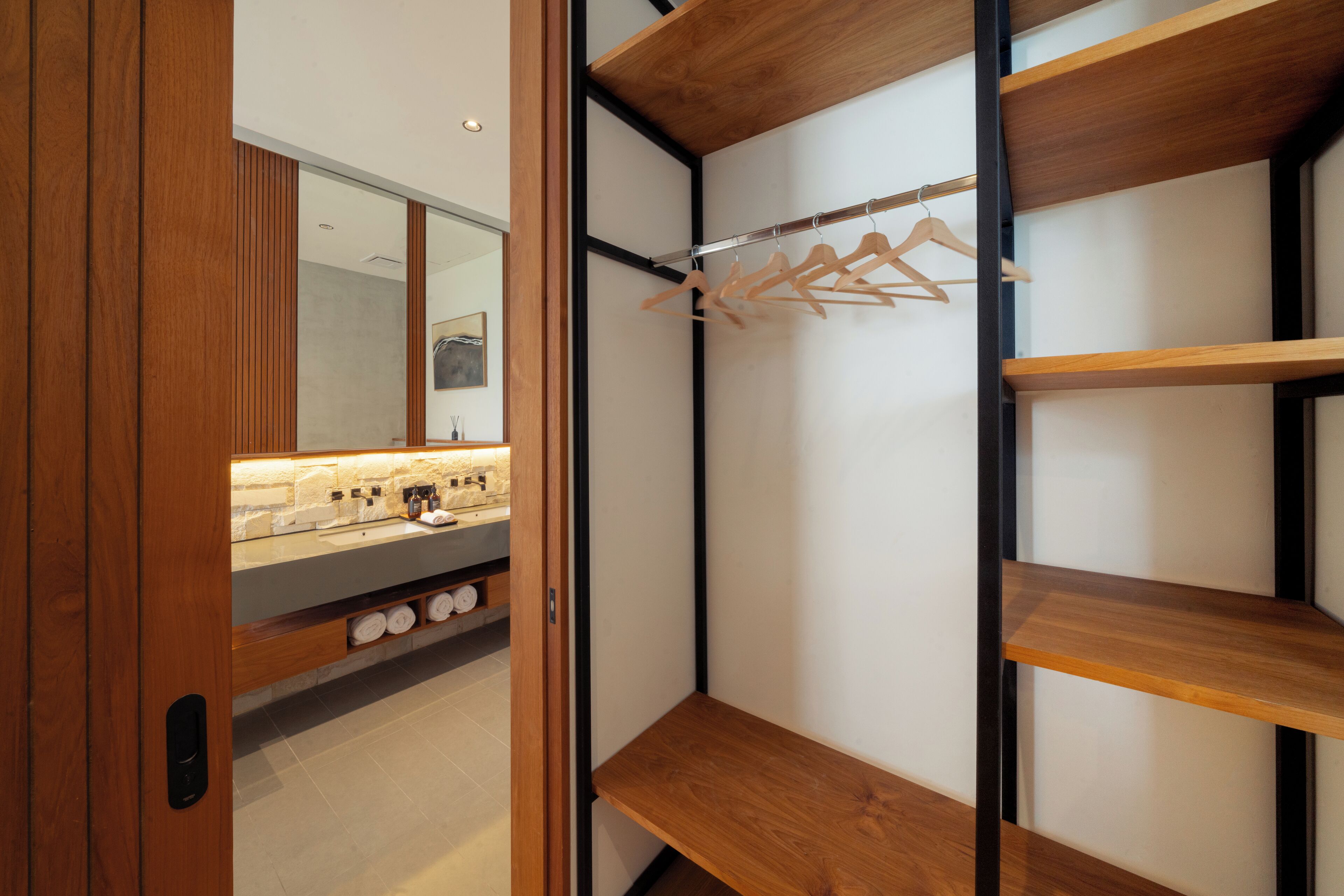 A modern bathroom with wooden shelving, a mirror, and a towel rack.