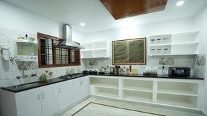 A modern kitchen with white cabinets, a black countertop, a gas stove, and a microwave. - Stylish 4-bedroom Family Getaway Luxury Living (Hyderabad)