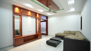 A modern living room with a wooden entertainment unit, a sofa, and a ceiling fan. - Stylish 4-bedroom Family Getaway Luxury Living (Hyderabad)