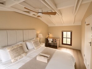 A bedroom with a bed, a desk, a chair, a ceiling fan, and a window.