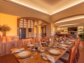 A long dining table set for a meal with multiple dishes and glasses, surrounded by wooden chairs.
