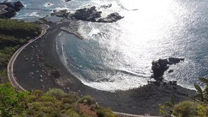 Uma estrada costeira sinuosa serpenteando por uma praia com afloramentos rochosos e vegetação.