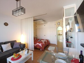 A cozy living room with a sofa, a dining table set with wine glasses and plates, a kitchen area with a stove, and a bedroom with a bed.