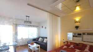 Quarto de hotel moderno com cama, sofá, área de refeições e cozinha compacta.