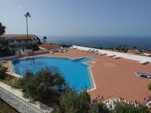 Una piscina con vistas despejadas al mar, rodeada de sillas de descanso y una valla blanca.