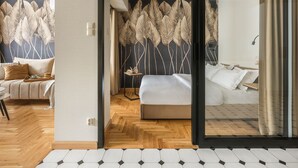 A modern hotel room with a wooden herringbone floor, a large bed with white bedding, a sofa with a beige throw, and a wall with a leaf pattern. - Art Palace by Fragola Collection (Kraków)