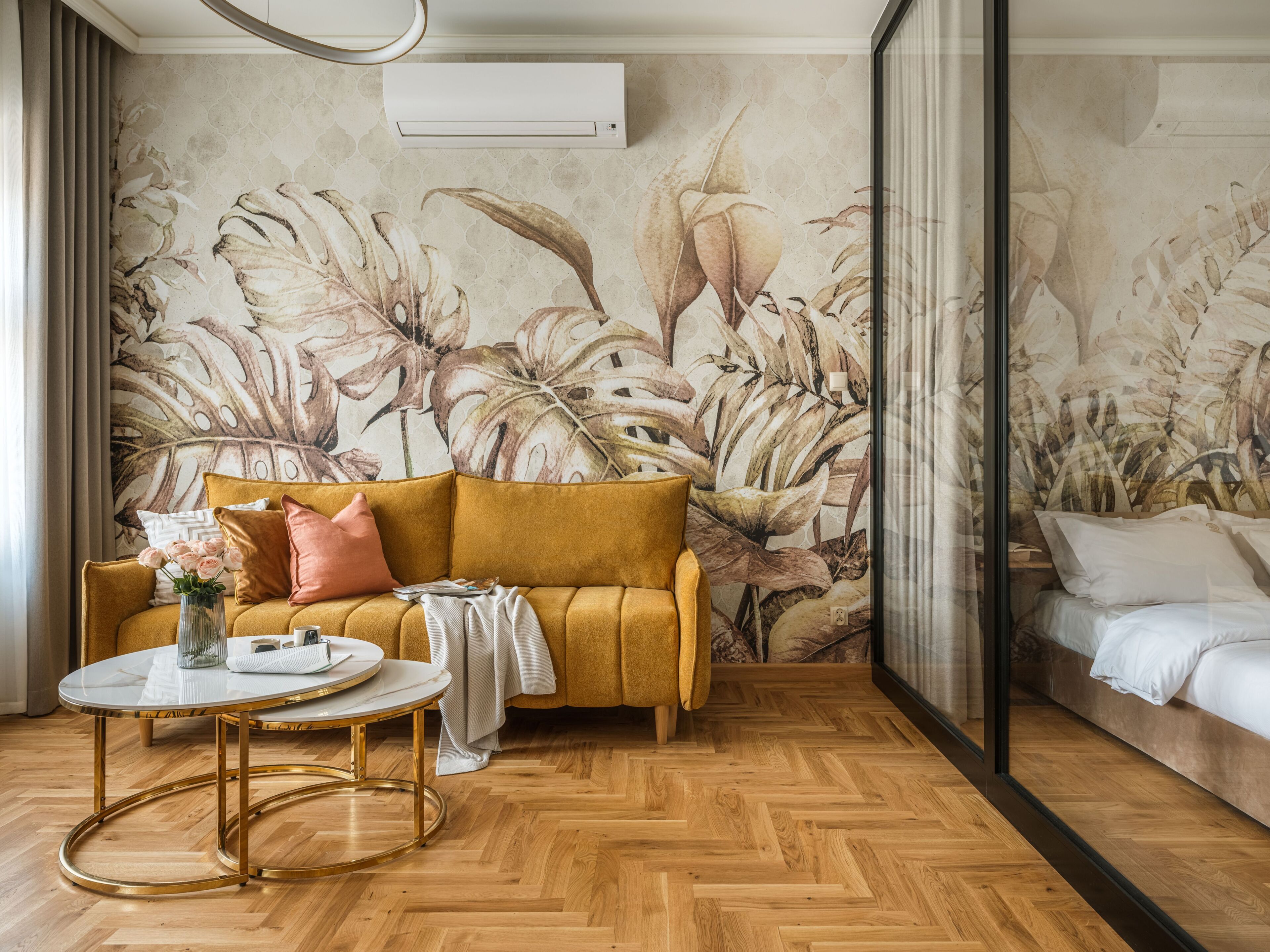 A room with a sofa, a round table, a bed, and a floral wall mural.