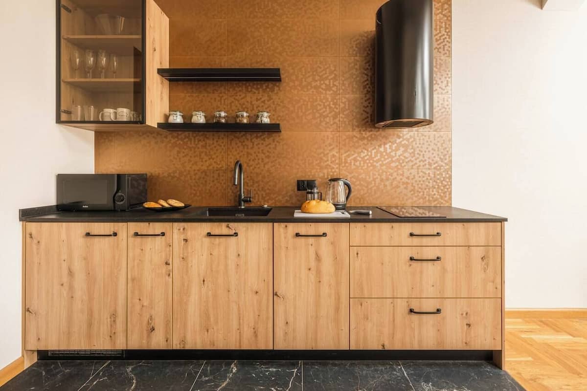 Una cocina moderna con armarios de madera, encimera negra, microondas integrado, cafetera y campana extractora negra.