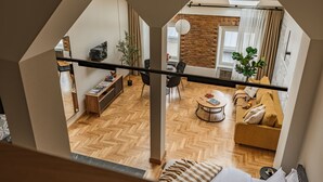 A modern loft-style apartment with a herringbone wood floor, a sofa, a dining area, and a brick accent wall. - Art Palace by Fragola Collection (Kraków)