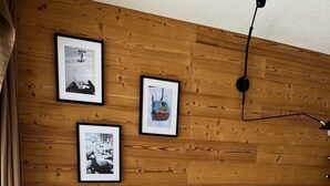 Un canapé gris avec trois coussins, un mur en bois orné de trois tableaux encadrés et un luminaire suspendu.