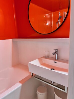 Un baño moderno con un lavamanos blanco, un espejo redondo y una bañera.
