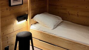 Un lit superposé avec une tête de lit, un petit tabouret et un tableau encadré accroché au mur.