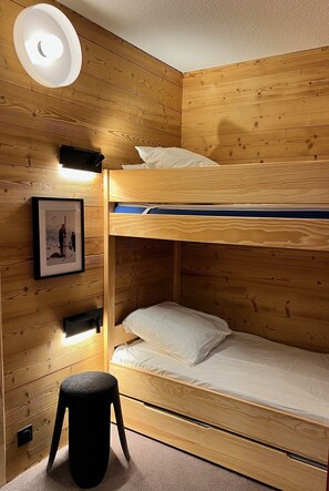 Una cama litera con cabecera, un taburete pequeño y un cuadro en la pared.